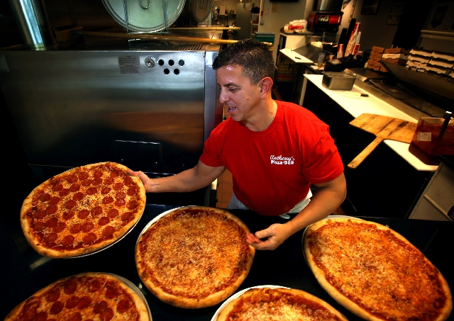 Anthony in an Anthony's Pizza & Deli shirt at the oven, surrounded by freshly baked pizzas